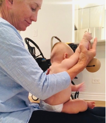 Dr. Tara Liddle supporting a baby through a stretch while seated on her lap.