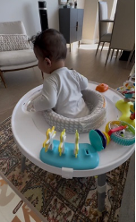 A baby sitting in a stationary activity center surrounded by toys.