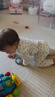 A baby on hands and knees crawling across a carpeted floor toward a toy.