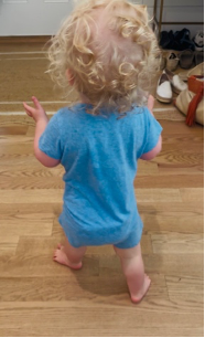 A toddler taking steps barefoot across a wooden floor.