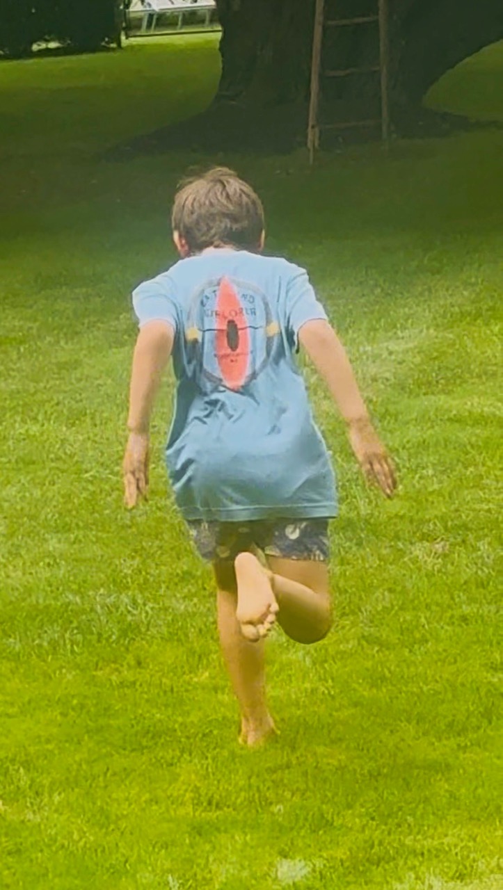 A child running barefoot across a lawn, seen from behind mid-stride.